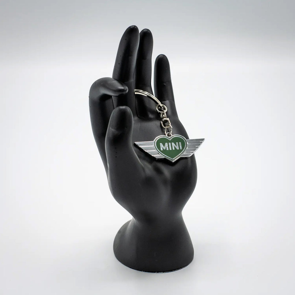 Keychain with a British Racing Green MINI heart design on a black mannequin hand against a white background.
