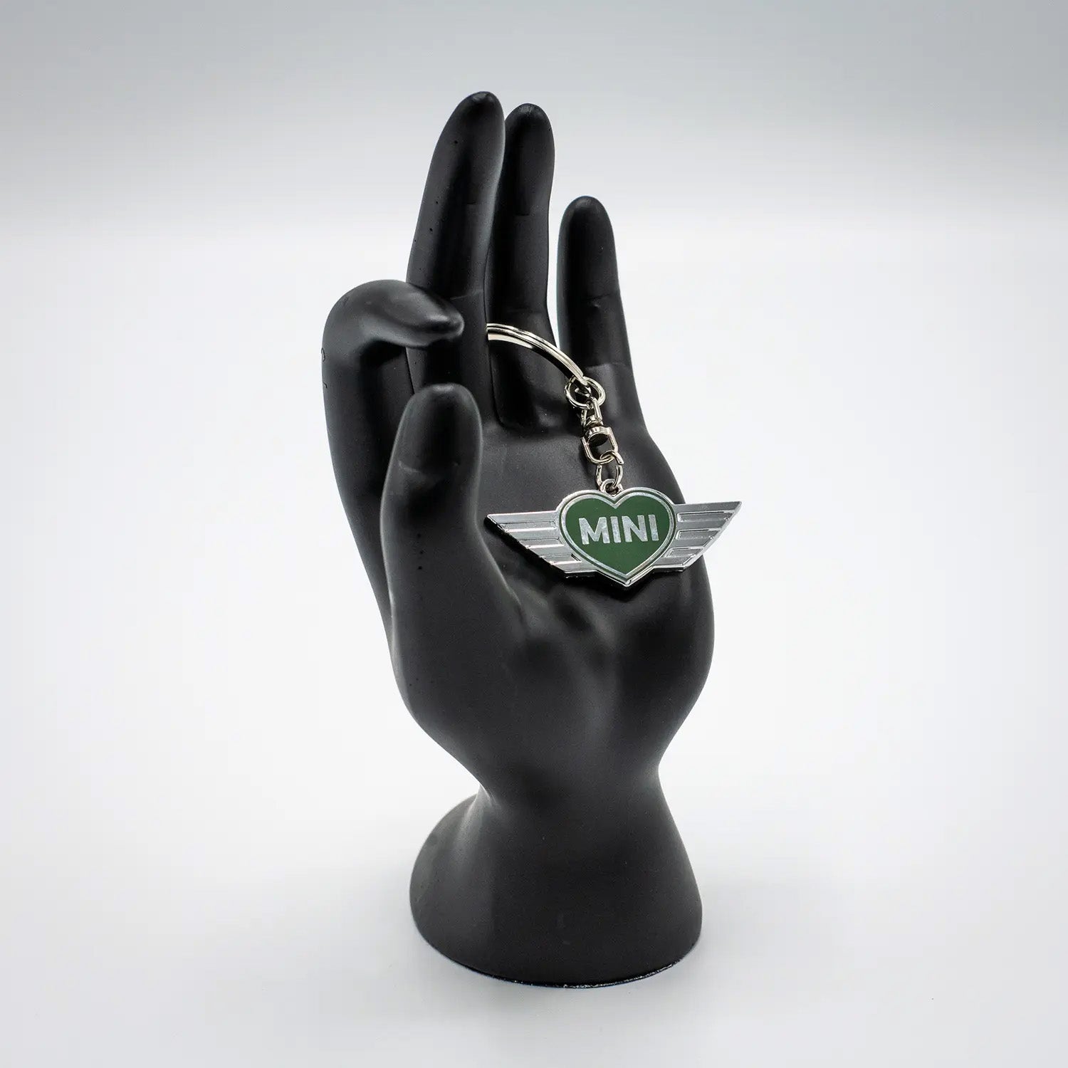 Keychain with a British Racing Green MINI heart design on a black mannequin hand against a white background.
