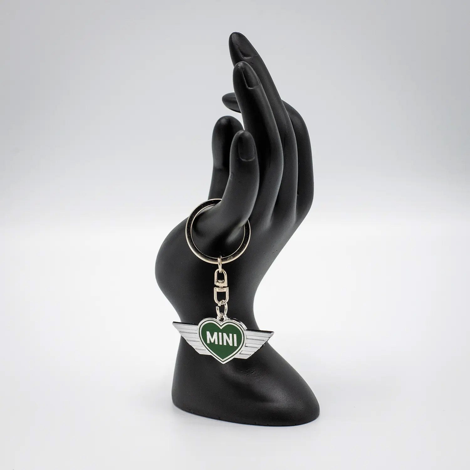Keychain with a British Racing Green MINI heart design on a black mannequin hand against a white background.