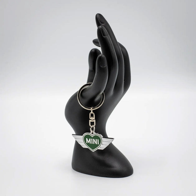 Keychain with a British Racing Green MINI heart design on a black mannequin hand against a white background.