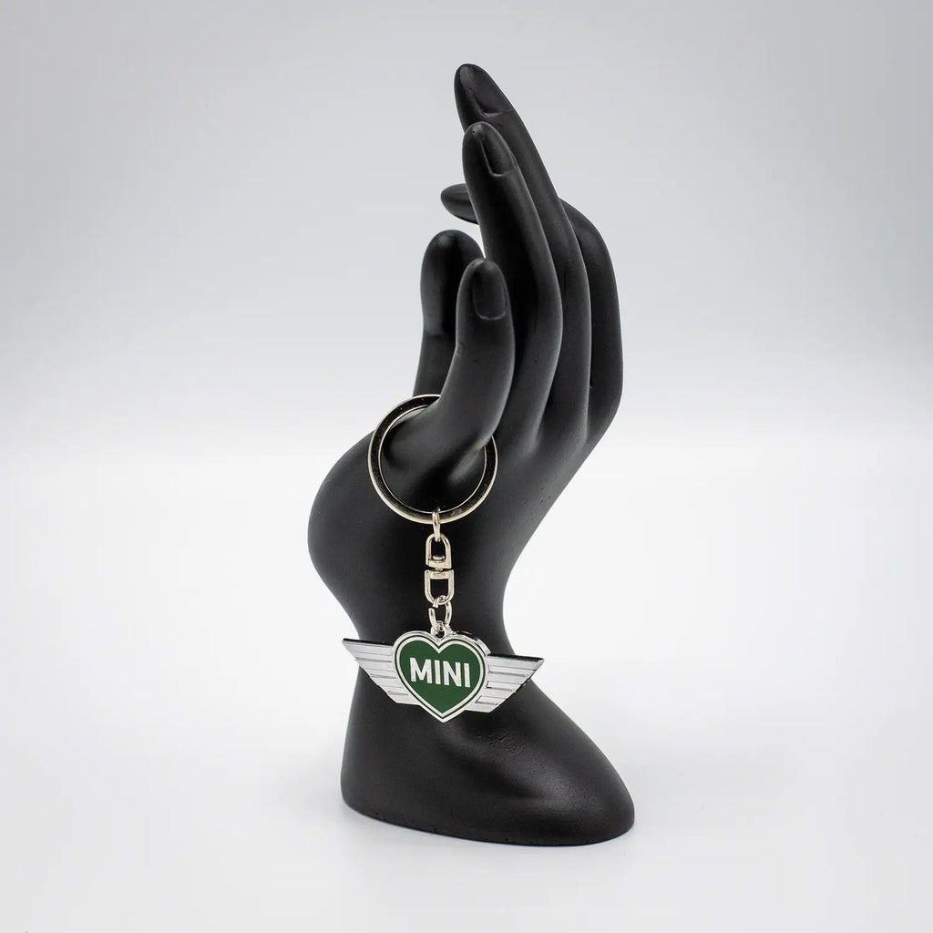 Keychain with a British Racing Green MINI heart design on a black mannequin hand against a white background.
