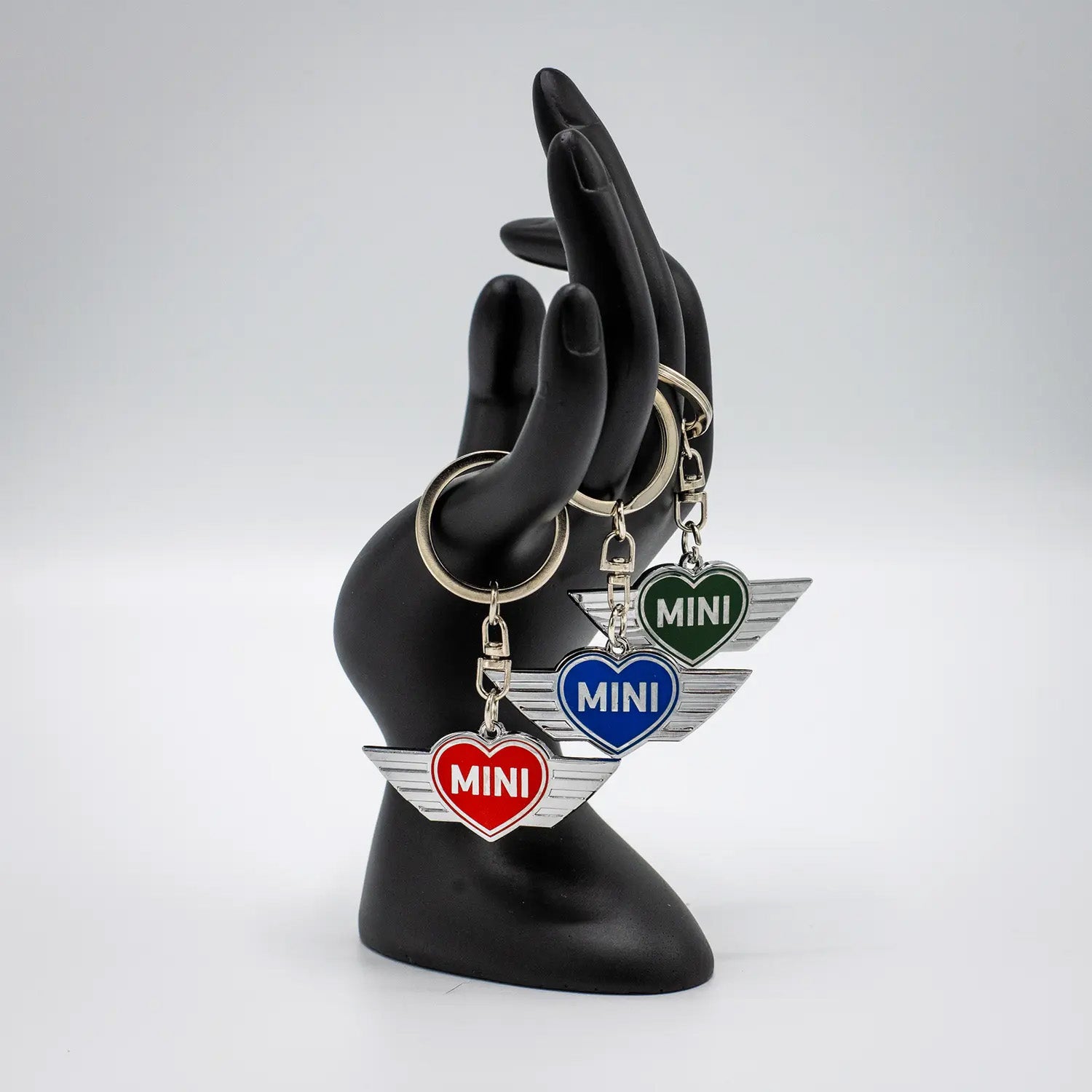 Black mannequin hand holding several MINI heart keychains on a white background.