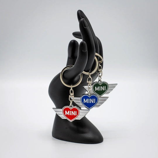 Black mannequin hand holding several MINI heart keychains on a white background.