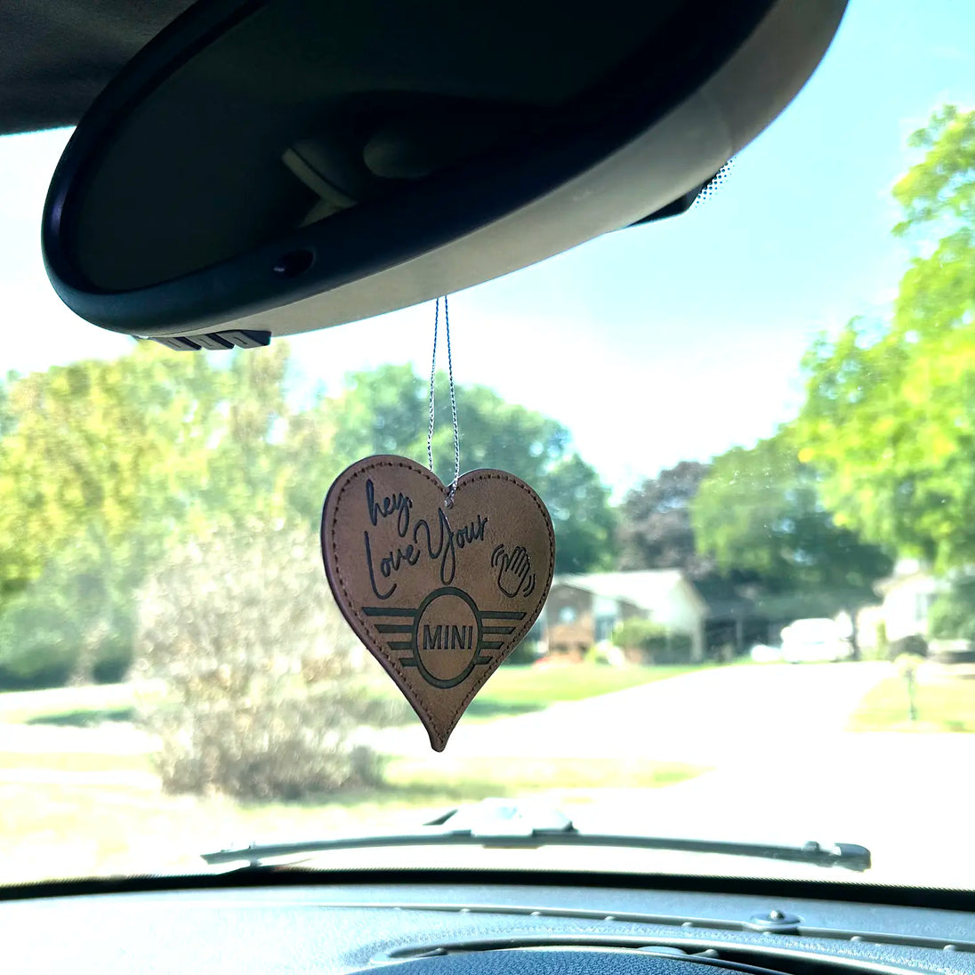 MINI Love Ducking Ornament hanging from a MINI's rearview mirror with a scenic background.